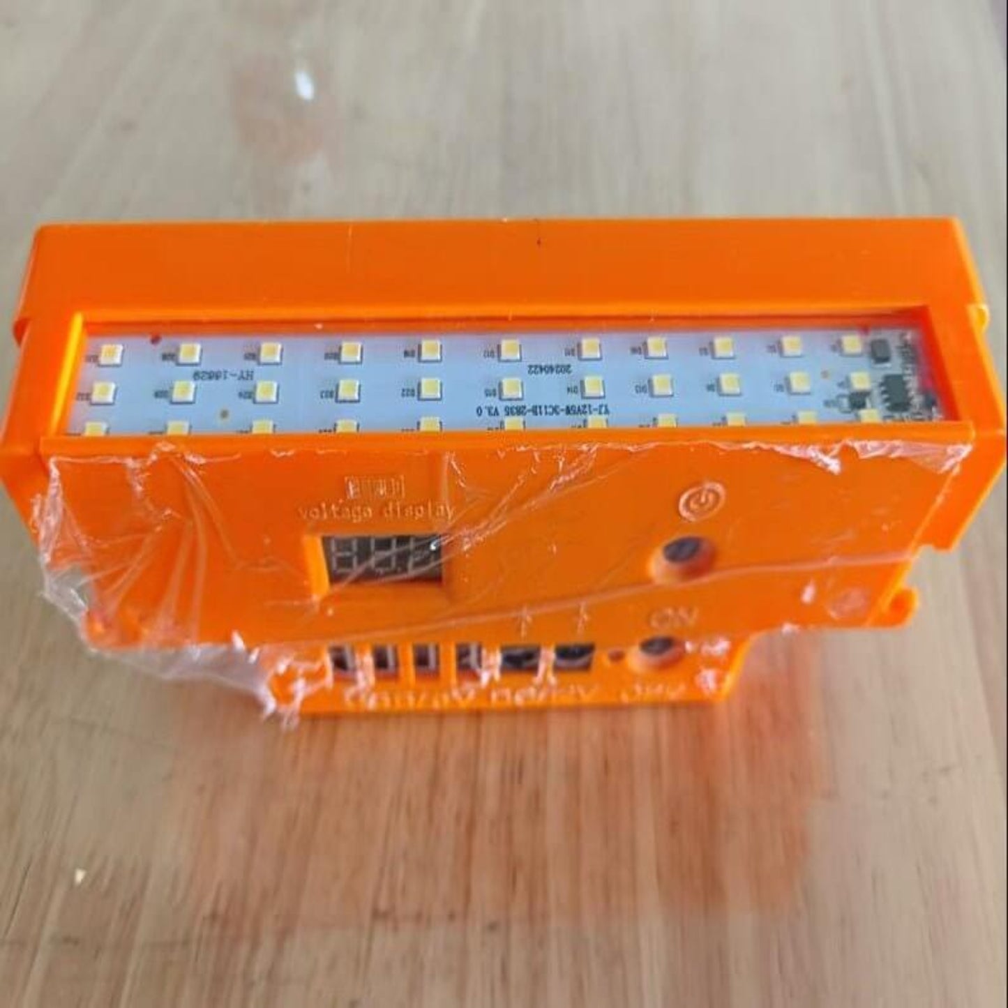 12V portable battery power bank prototype with LED lights, orange casing, and digital voltage display.