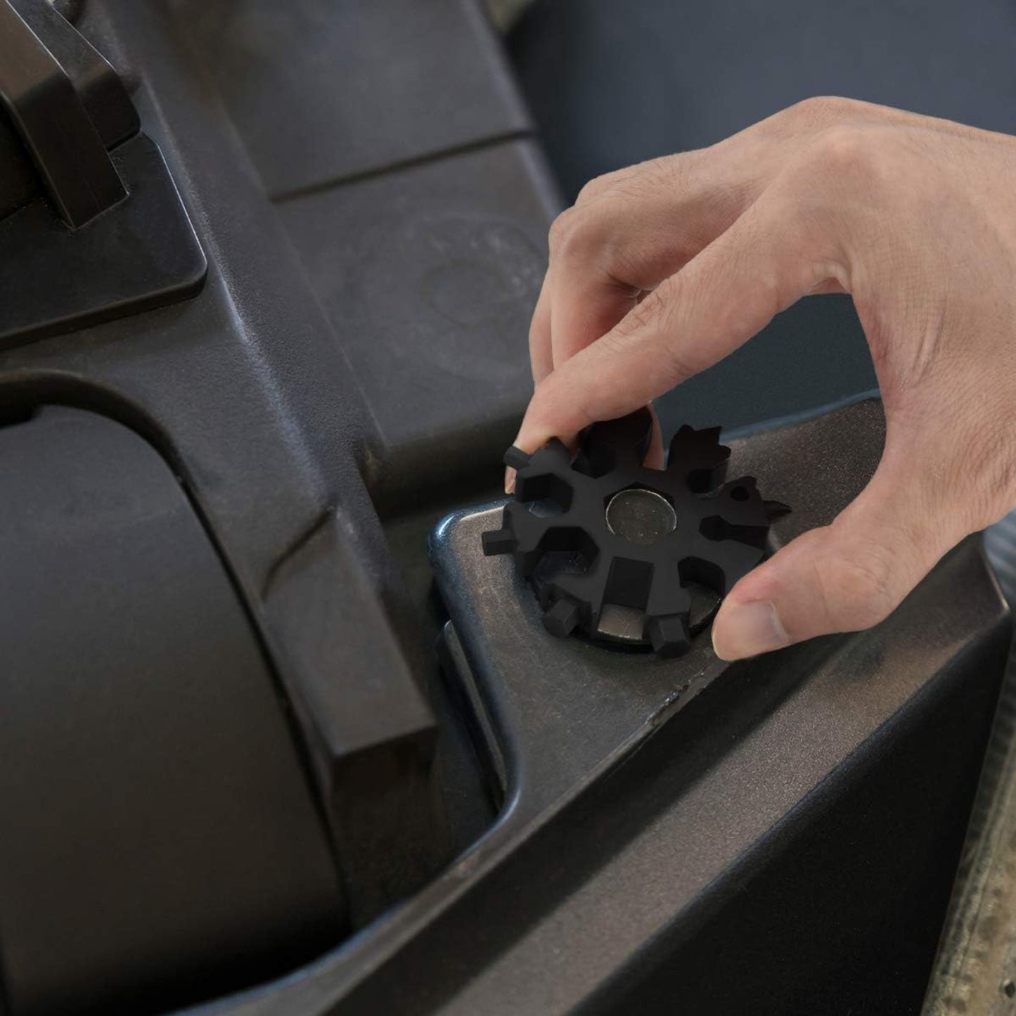 Hand placing the 18-in-1 snowflake multi-tool on a gray surface, showcasing its compact design and versatility.