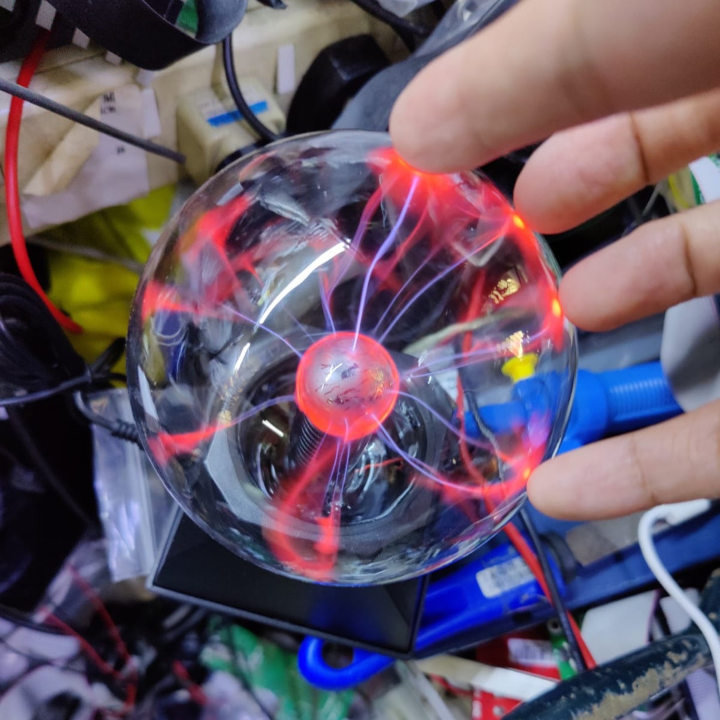 Hand reaching towards a 4-inch USB Plasma Ball, showcasing electric arcs and vibrant colors on a cluttered desk.