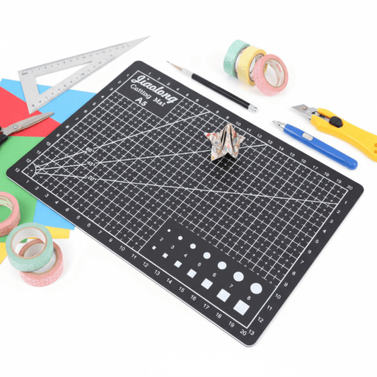 Cutting mat with grid lines surrounded by scissors, tape, and other tools on a white background