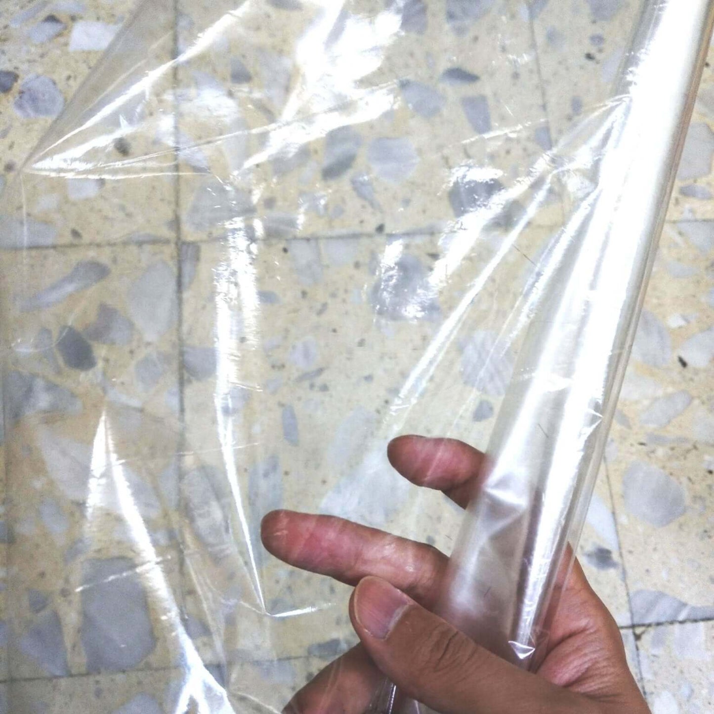 Hand holding a roll of clear heat shrink wrap film on a textured surface, ideal for packaging gifts and products.
