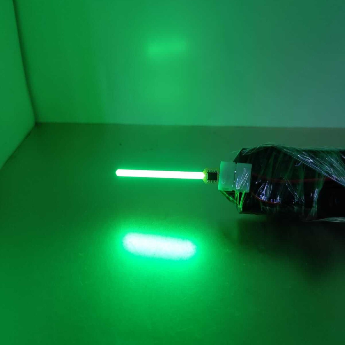 Green LED light emitting from a sleek tube lamp, showcasing vibrant glowing effect on a reflective surface.