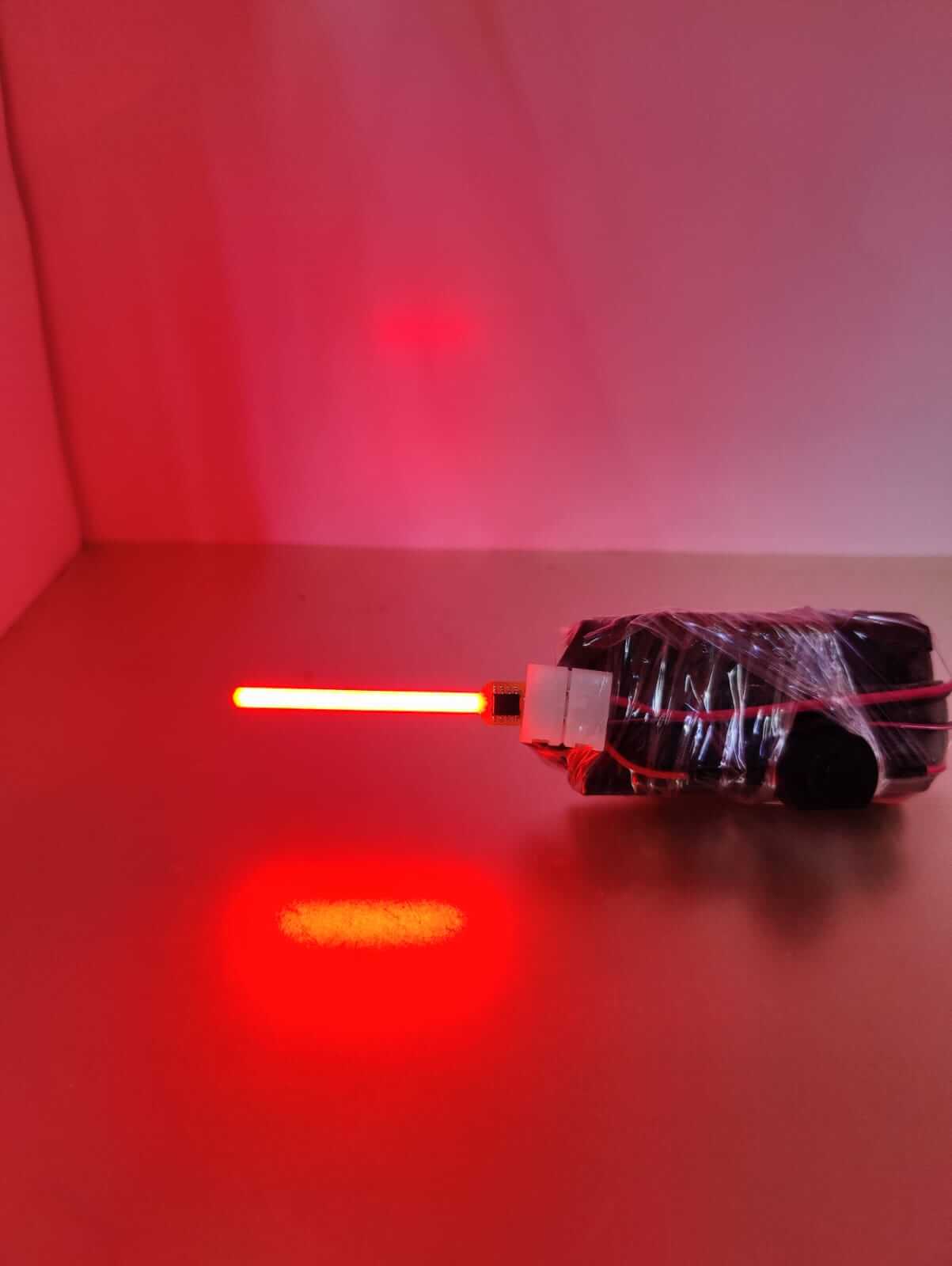 Red illuminated LED light wand wrapped in black tape on a reflective surface.