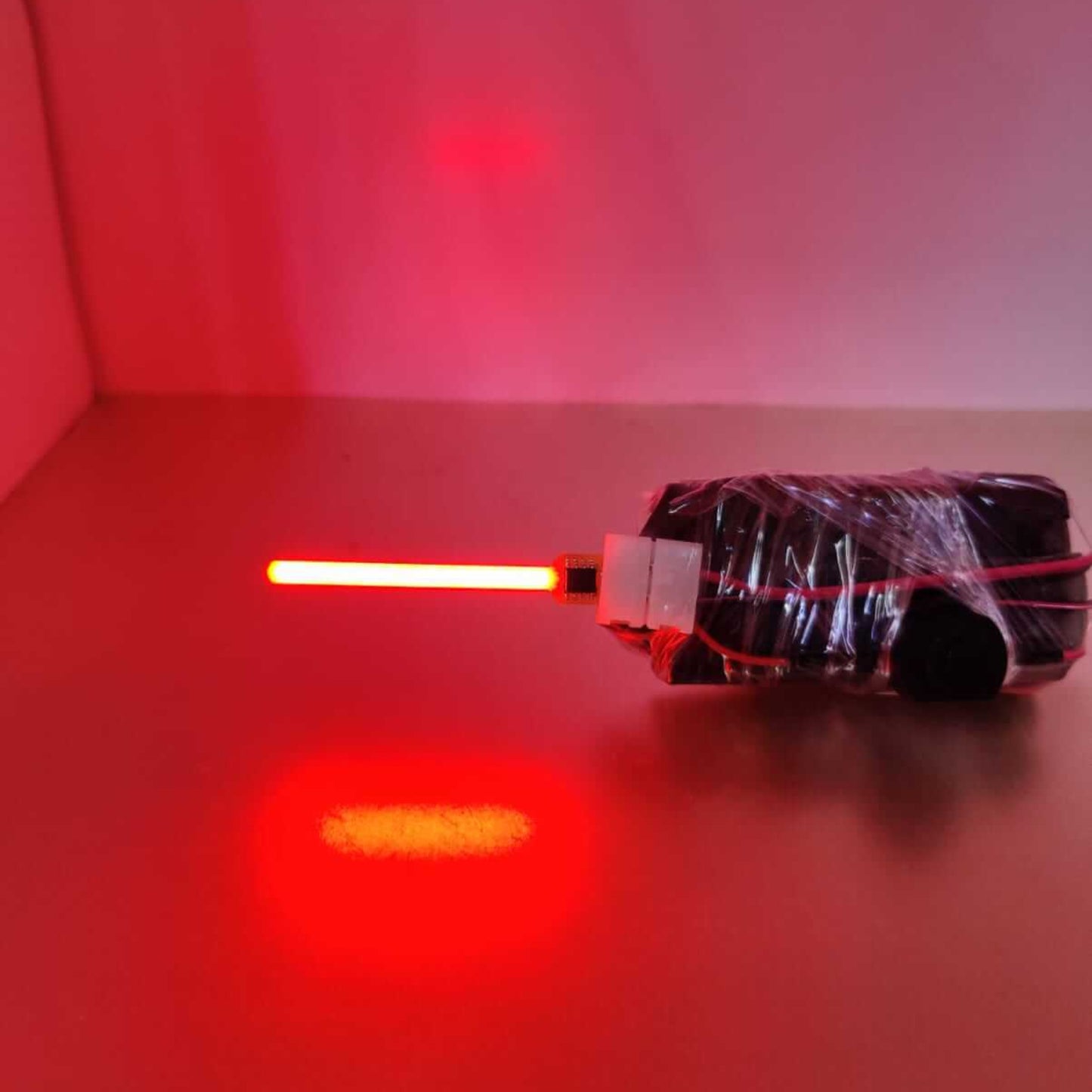 Red illuminated LED light wand wrapped in black tape on a reflective surface.