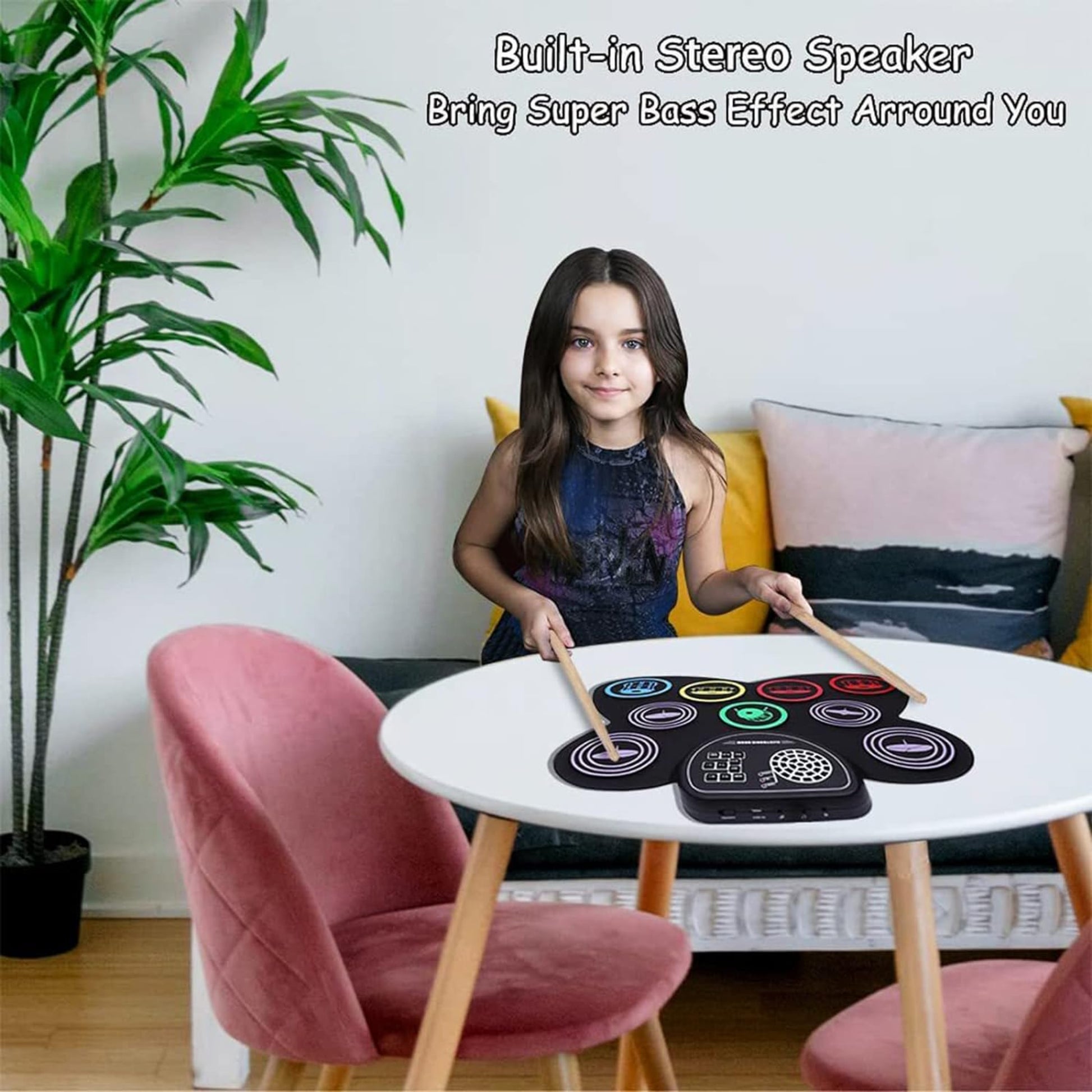 Girl playing on a portable 9-pad electronic drum set with built-in stereo speaker at a table in a stylish room.