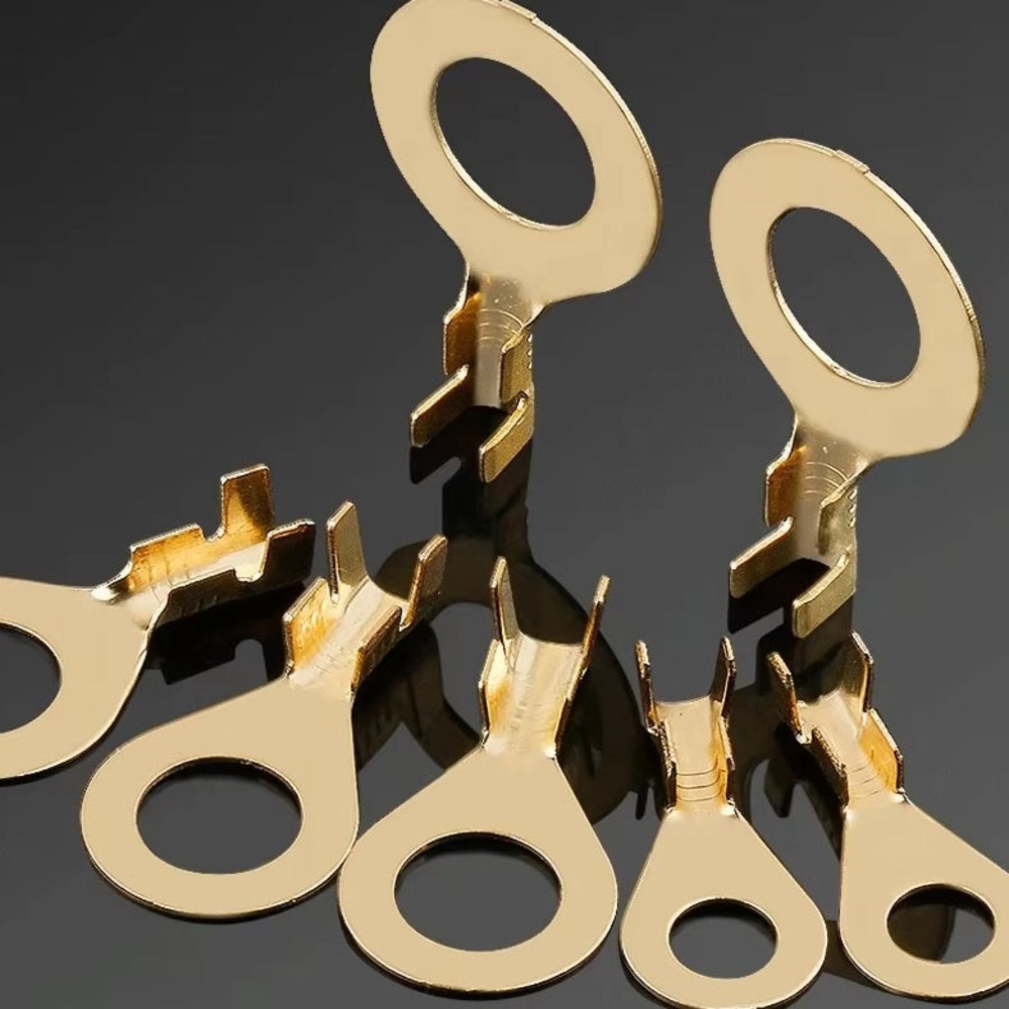 A close-up macro photo displaying various sizes of golden brass ring terminals from the assortment kit.