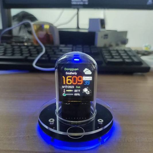 Nixie tube style smart clock on a desktop, showing Dongguan weather with a clear base and blue LED backlight.