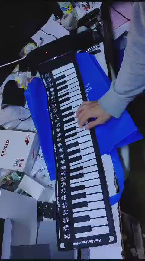 Person playing a 49-key roll-up piano keyboard on a table with various items around.
