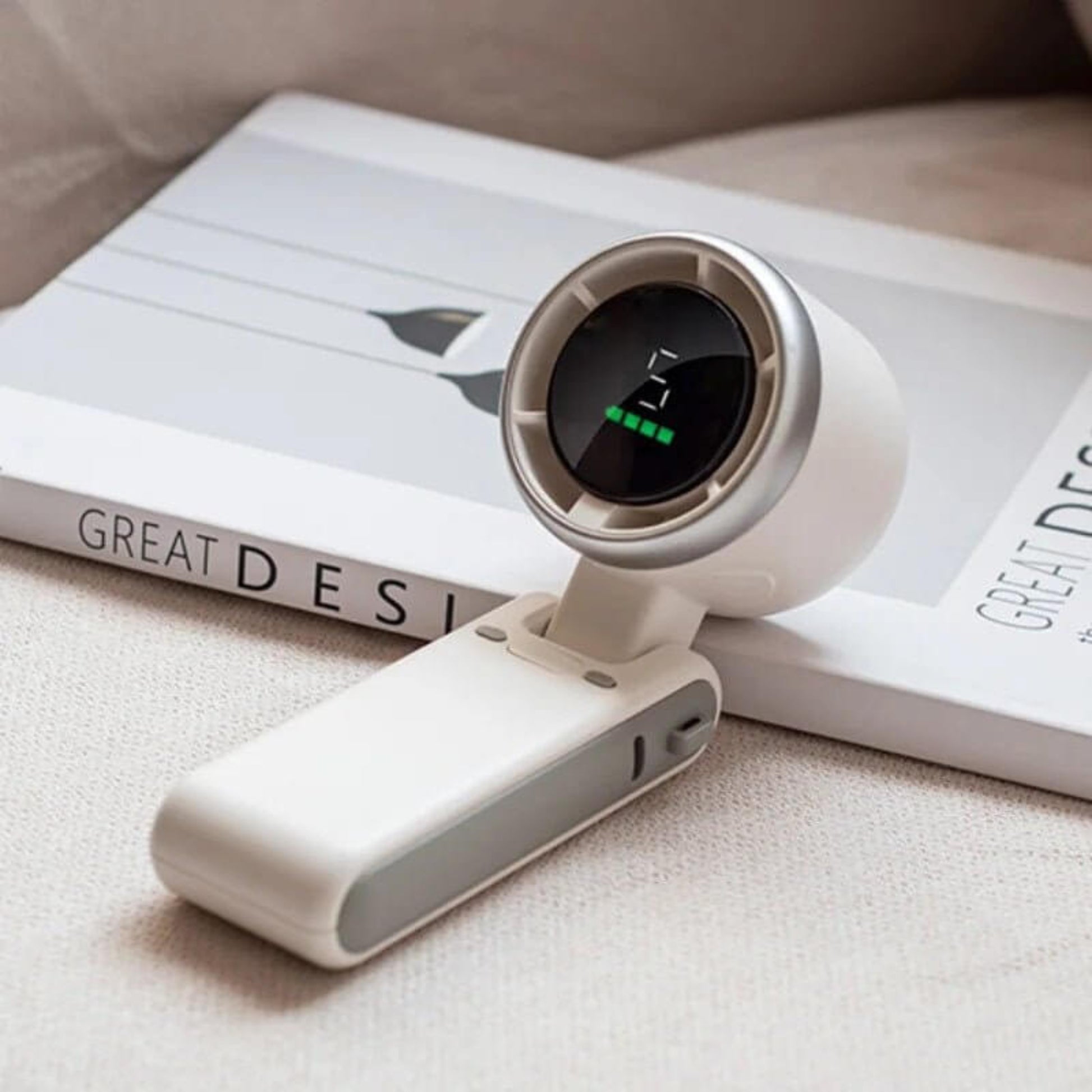 White mini turbo fan folded and resting on a book, showing the display with battery and fan speed indicator.