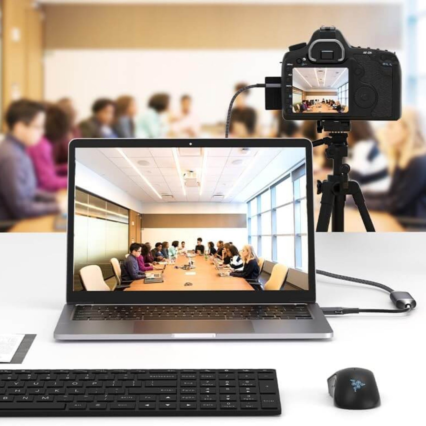Laptop displaying a video call with a camera capturing a meeting in a conference room setting.
