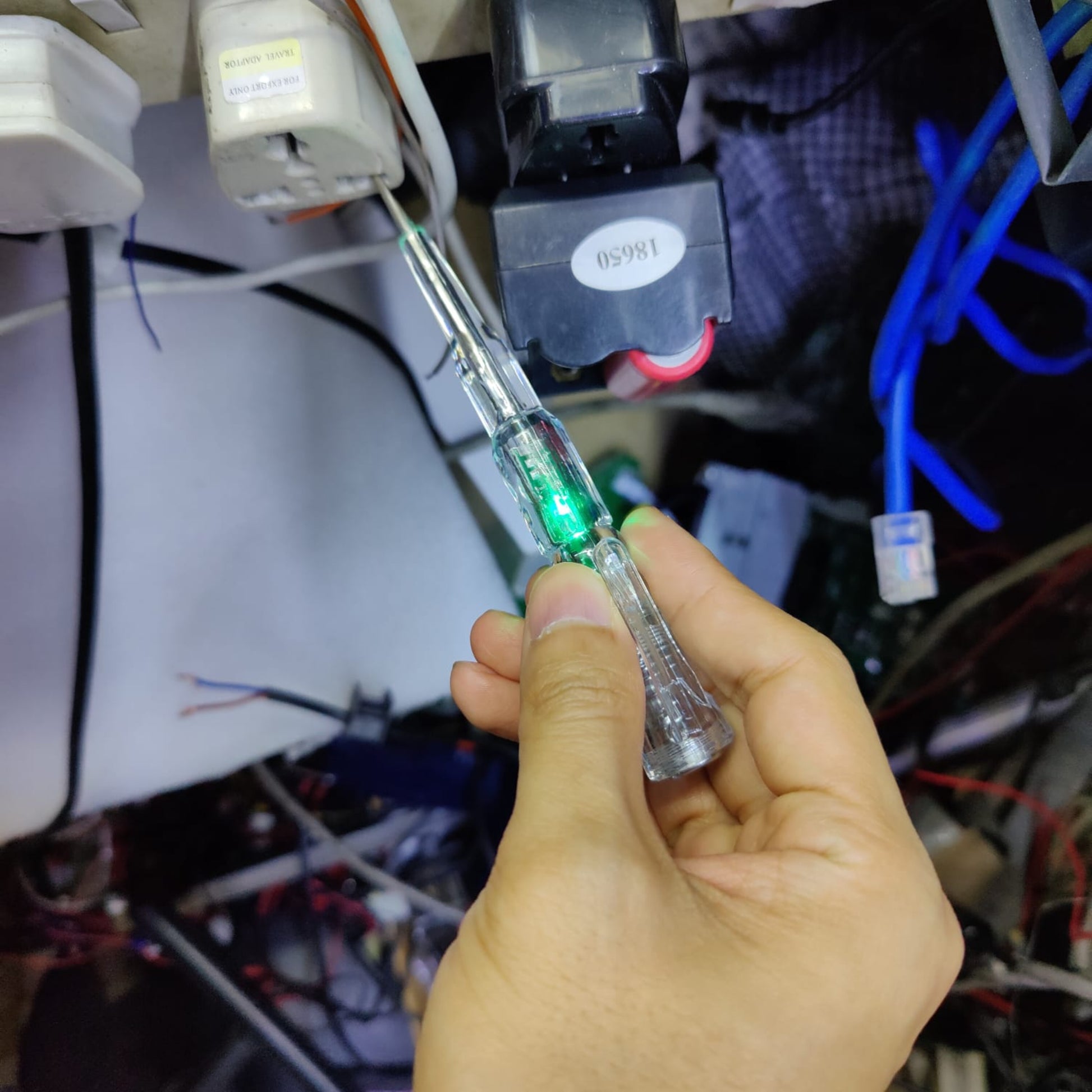 A hand holding a voltage tester pen, which is glowing green to indicate a live electrical socket.
