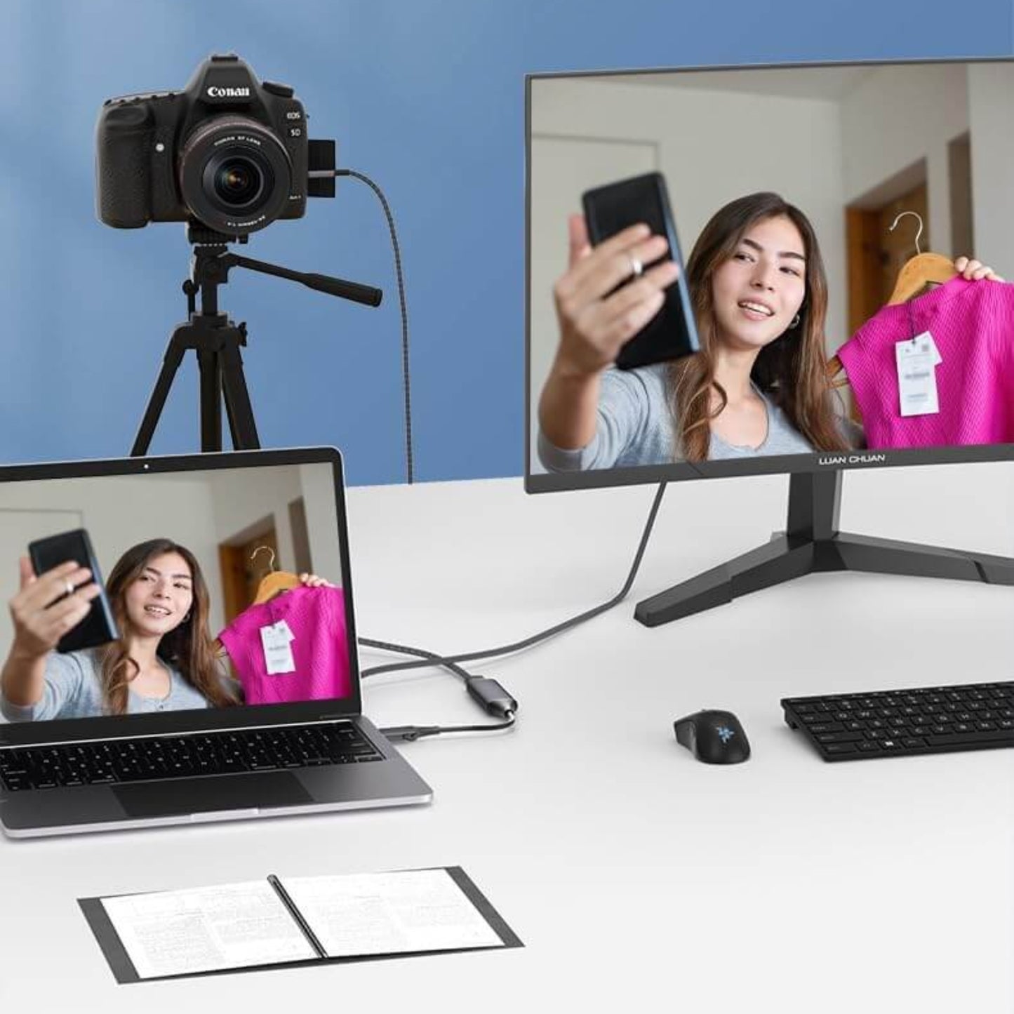 Woman presenting a pink garment while using a laptop and a camera for video streaming, showcasing a modern home setup.