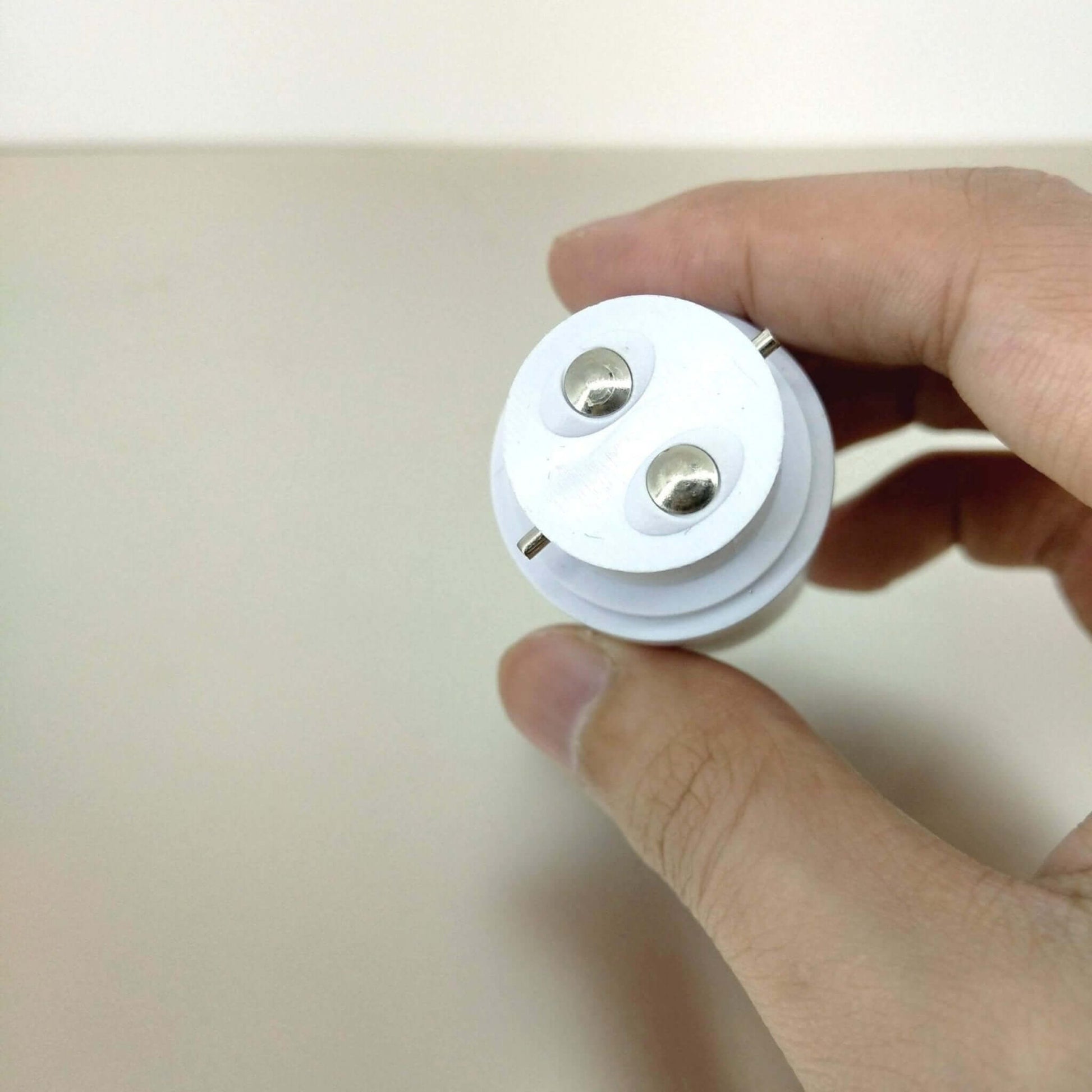 Hand holding a B22 to E27 light socket adapter converter for upgrading lighting fixtures.