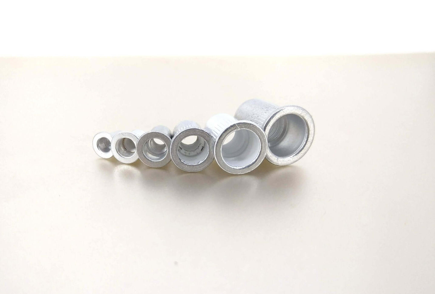Various sizes of aluminum rivet nuts displayed in a row, showcasing the M3-M10 threaded insert kit.