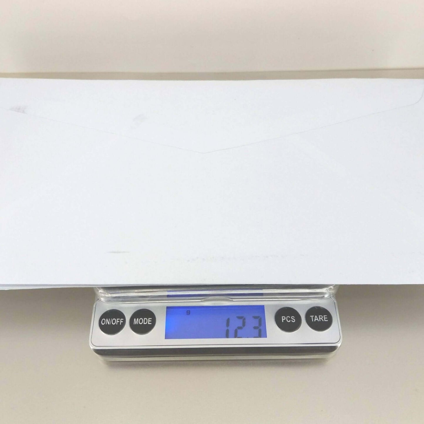 Digital pocket scale showing weight of 123g with an envelope on top, demonstrating high precision and accuracy.