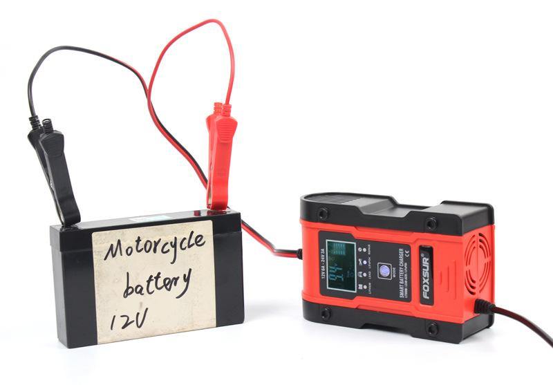 FOXSUR smart battery charger connected to a 12V motorcycle battery, displaying a voltage reading on its screen.
