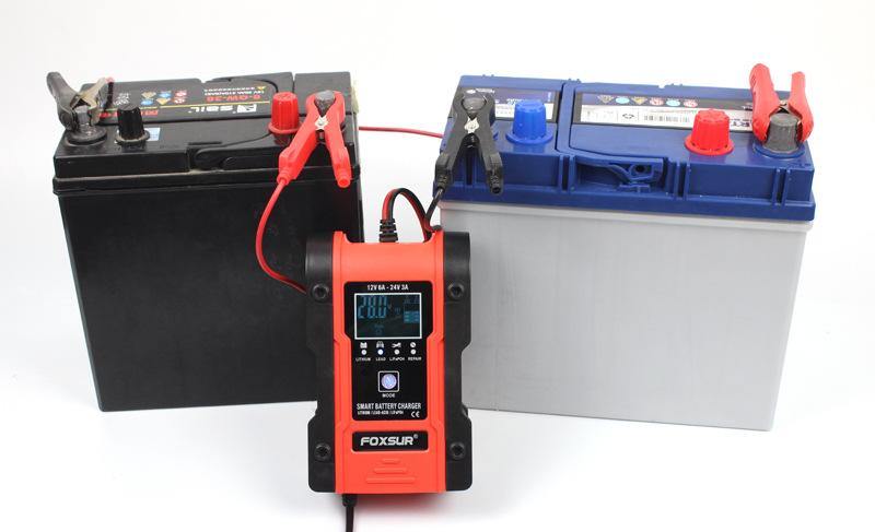 FOXSUR smart battery charger connected to two different car batteries, displaying a 20.0V reading, possibly indicating a 24V charging mode.