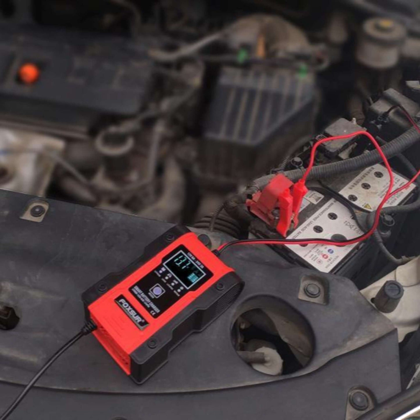 Foxsur 12V/24V Smart Battery Charger connected to a car battery under the hood, charging.