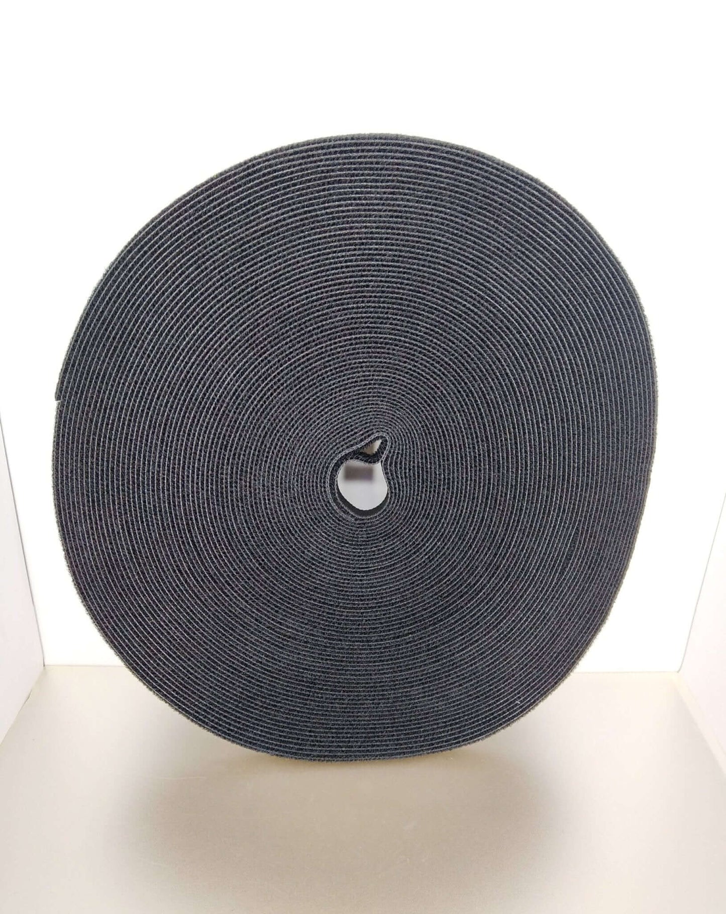 1cm x 25m self-adhesive hook and loop fastener cable ties in a circular roll, ideal for organizing cables and wires.