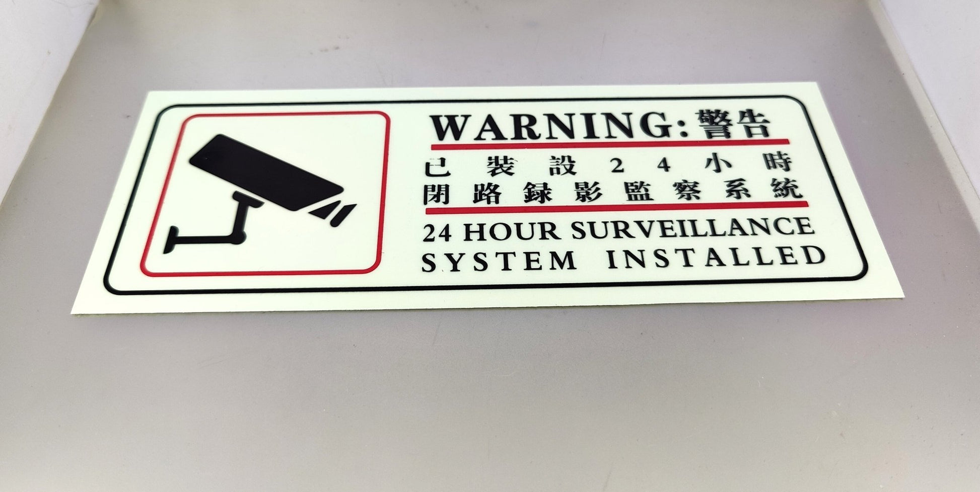 Clear front view of luminous security camera warning sticker for property and business protection.