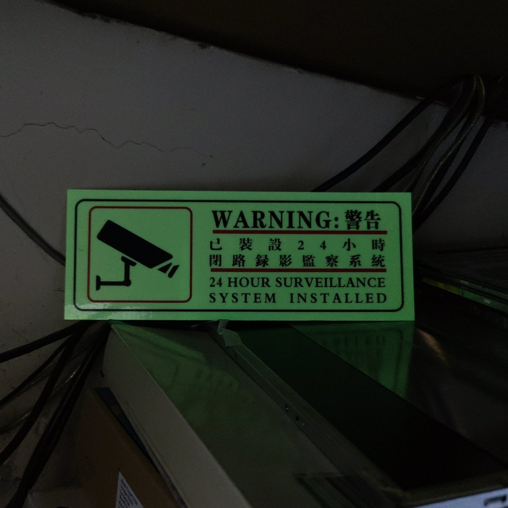 Luminous CCTV warning sticker glowing brightly at night, indicating active 24-hour video surveillance.