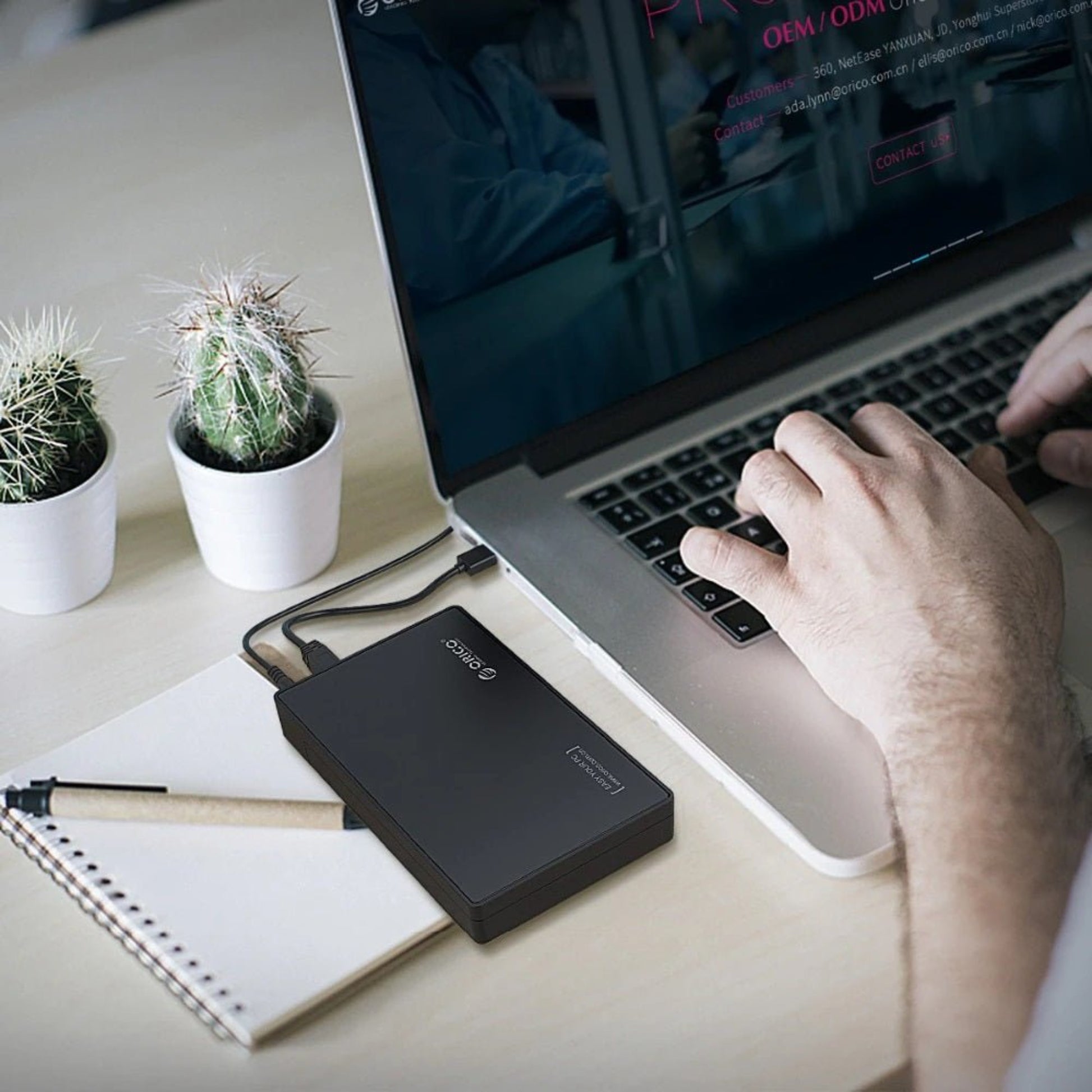 Person using a laptop with ORICO 3588US3 3.5" SATA HDD enclosure on the desk, showcasing productivity and modern work setup.