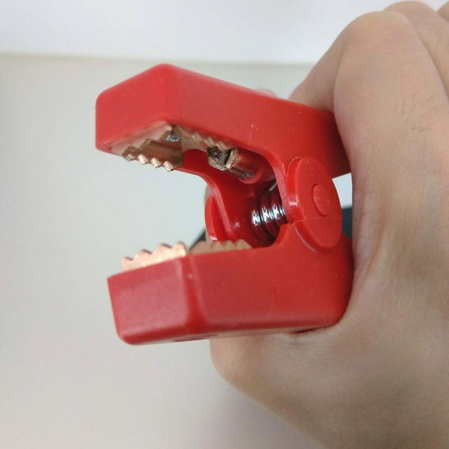 Close-up of red alligator clip used for battery jumper cables, showing strong grip and metal teeth for connection.