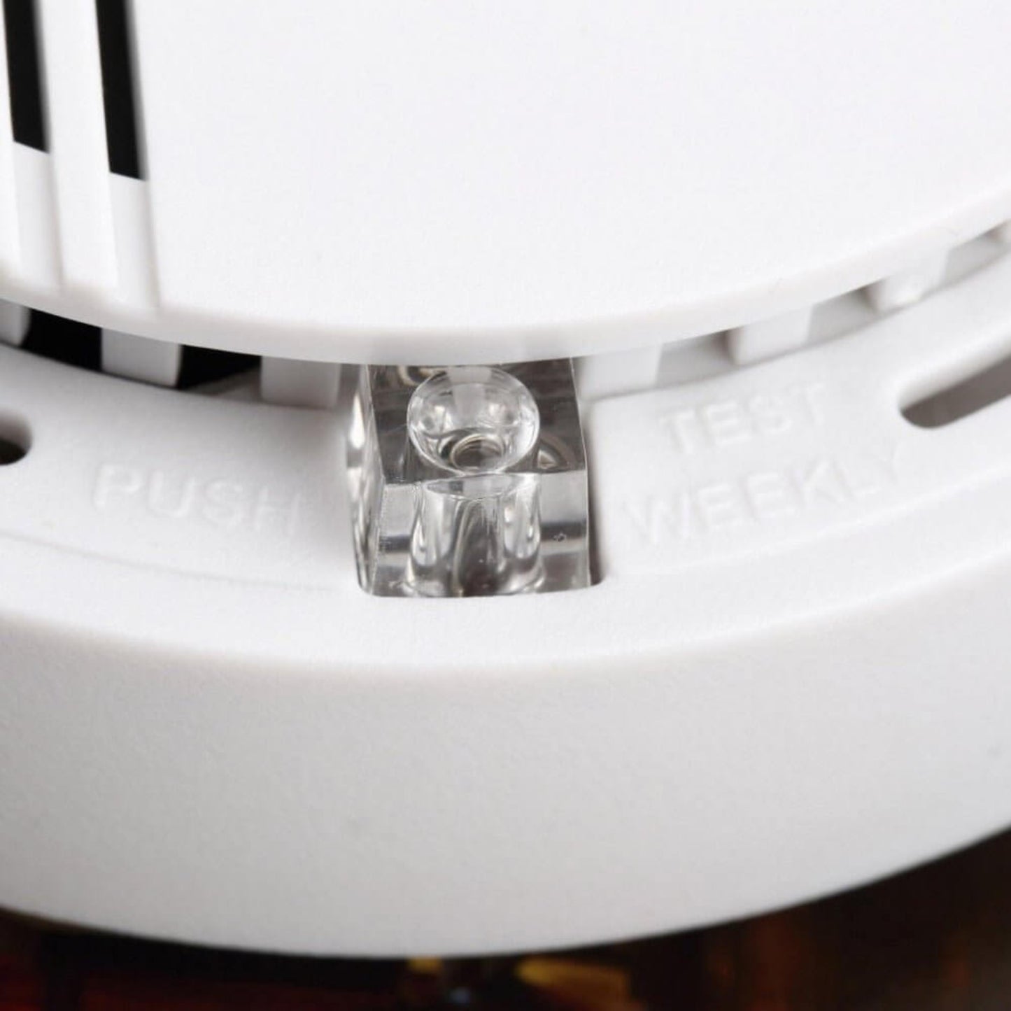 Close-up of a smoke alarm, clearly showing "PUSH TEST WEEKLY" text and the test button for routine checks.