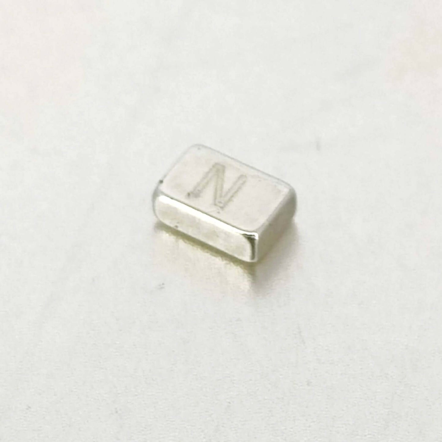 Strong mini rectangular magnet 6x4x2mm with 'N' marking on a smooth surface, ideal for DIY and organizing.