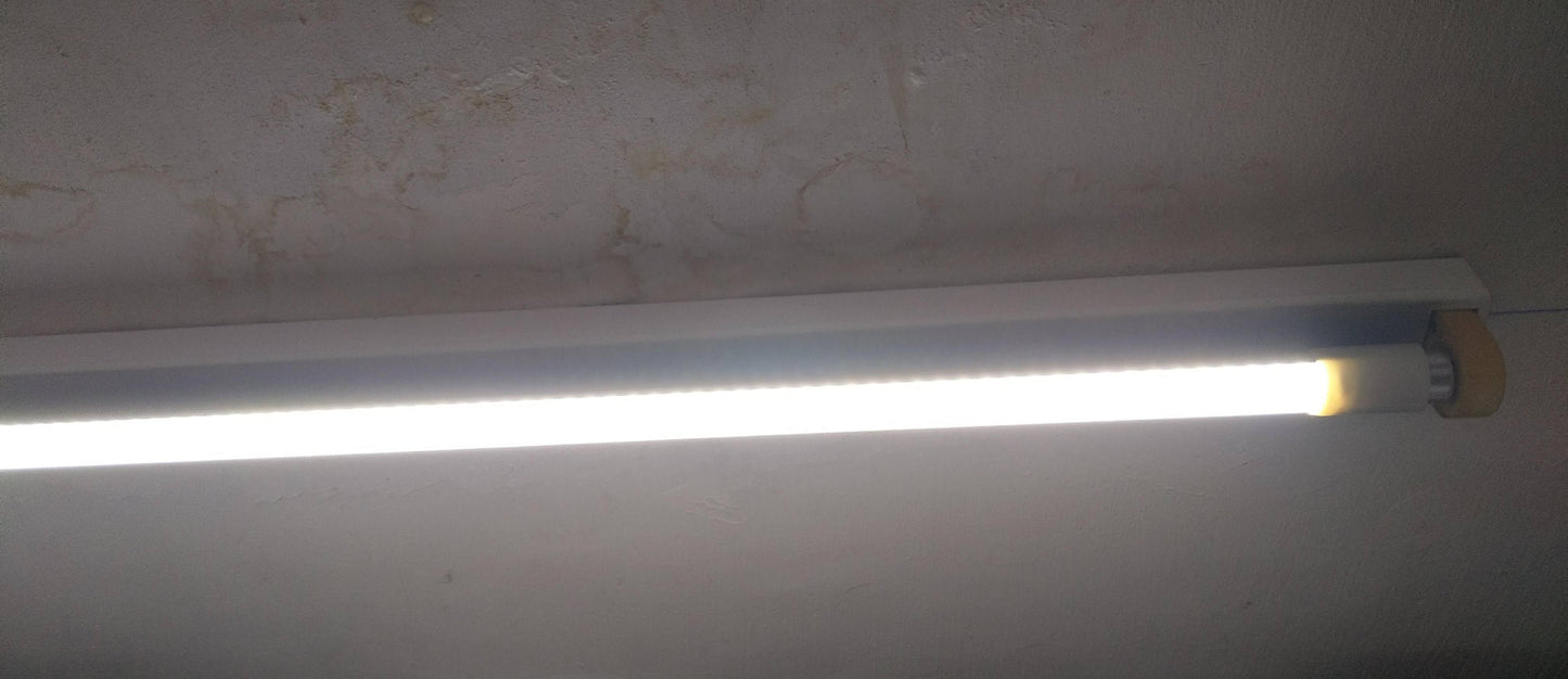 An illuminated T8 48-inch LED tube light installed in a ceiling fixture, emitting bright cool white light into the room.