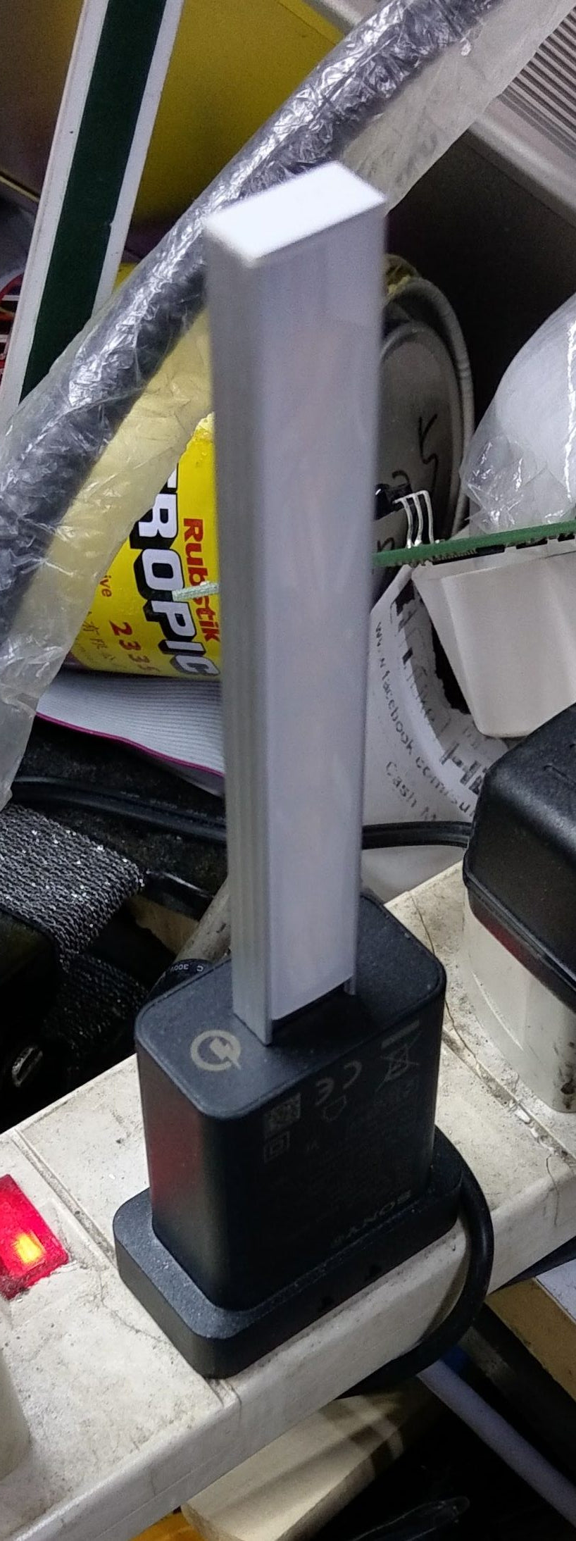 Portable USB stick LED light, turned off, plugged into a black USB charger