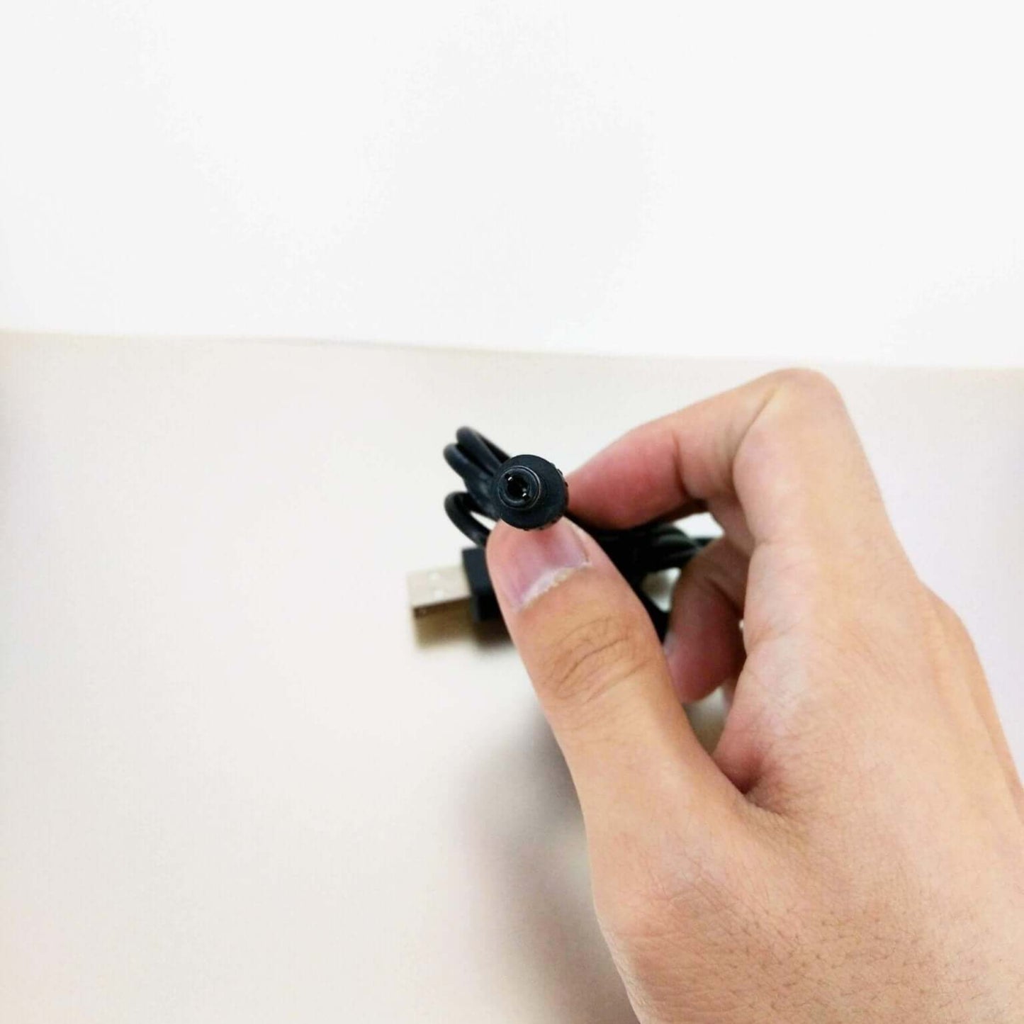 Hand holding a USB 5V to 12V DC step-up voltage converter cable with a 5.5mm x 2.1mm connector.