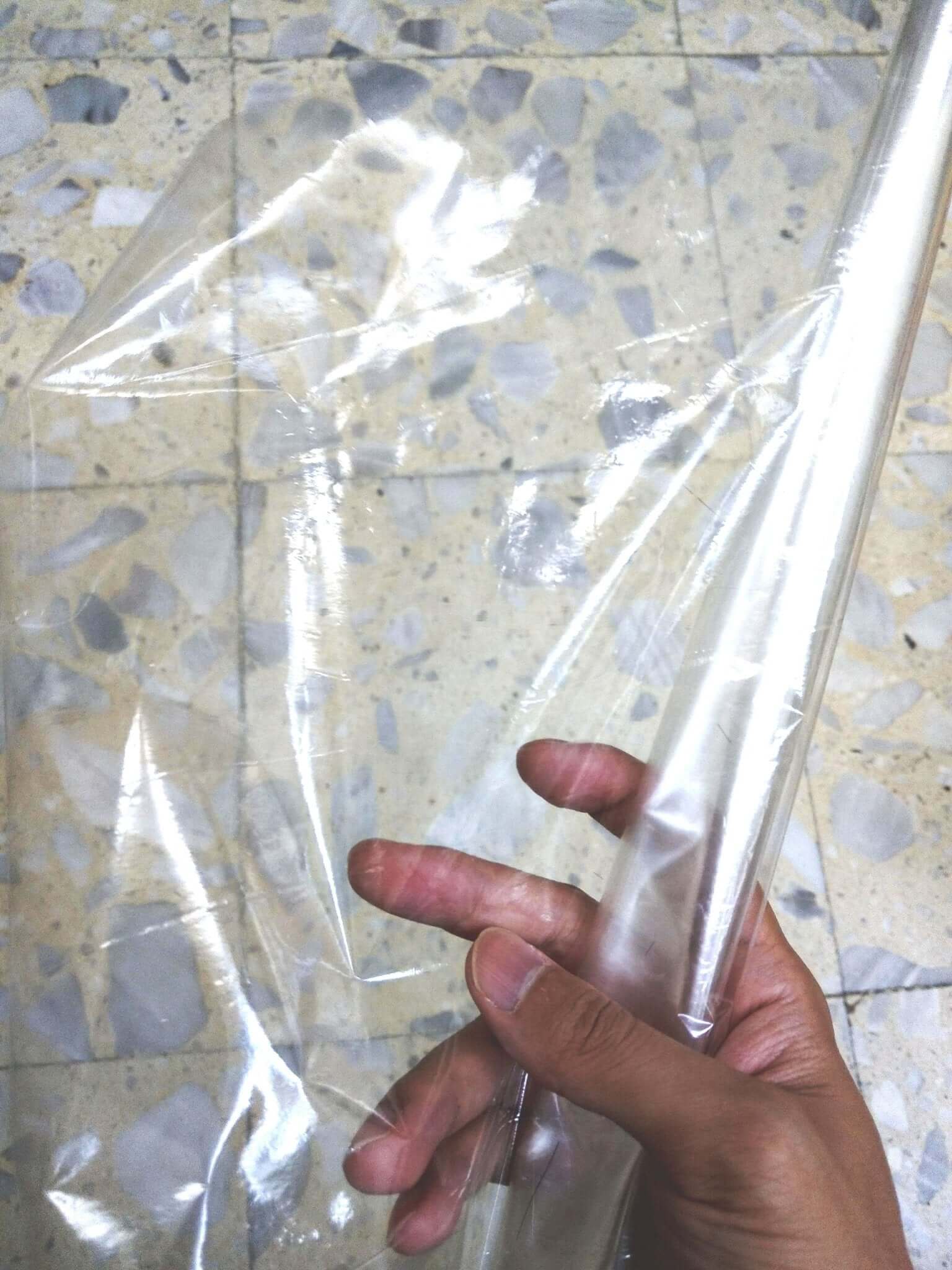 Hand holding a roll of heat shrink wrap film on a textured floor, showcasing the clear packaging solution.