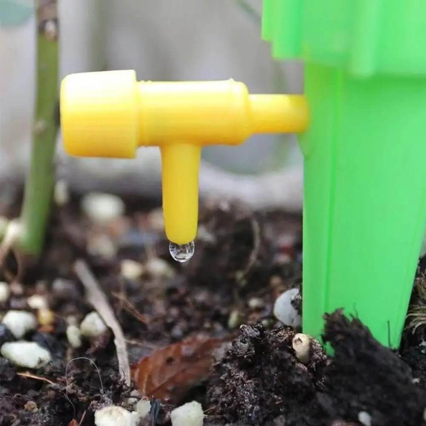 Close-up of yellow automatic drip watering spike releasing a drop of water in soil near plant.