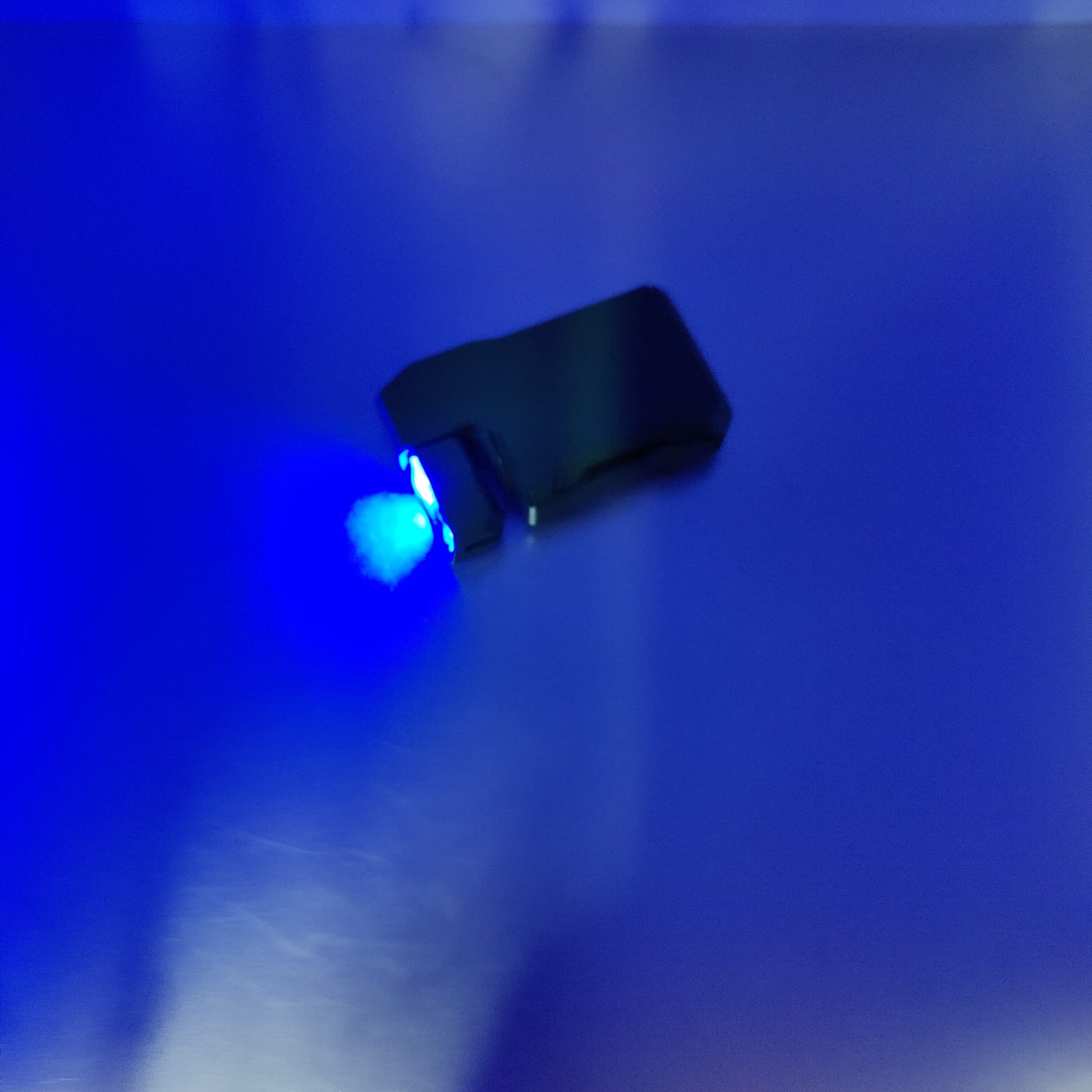 The tactical black EDC mini flashlight illuminating a surface with its bright blue light mode.