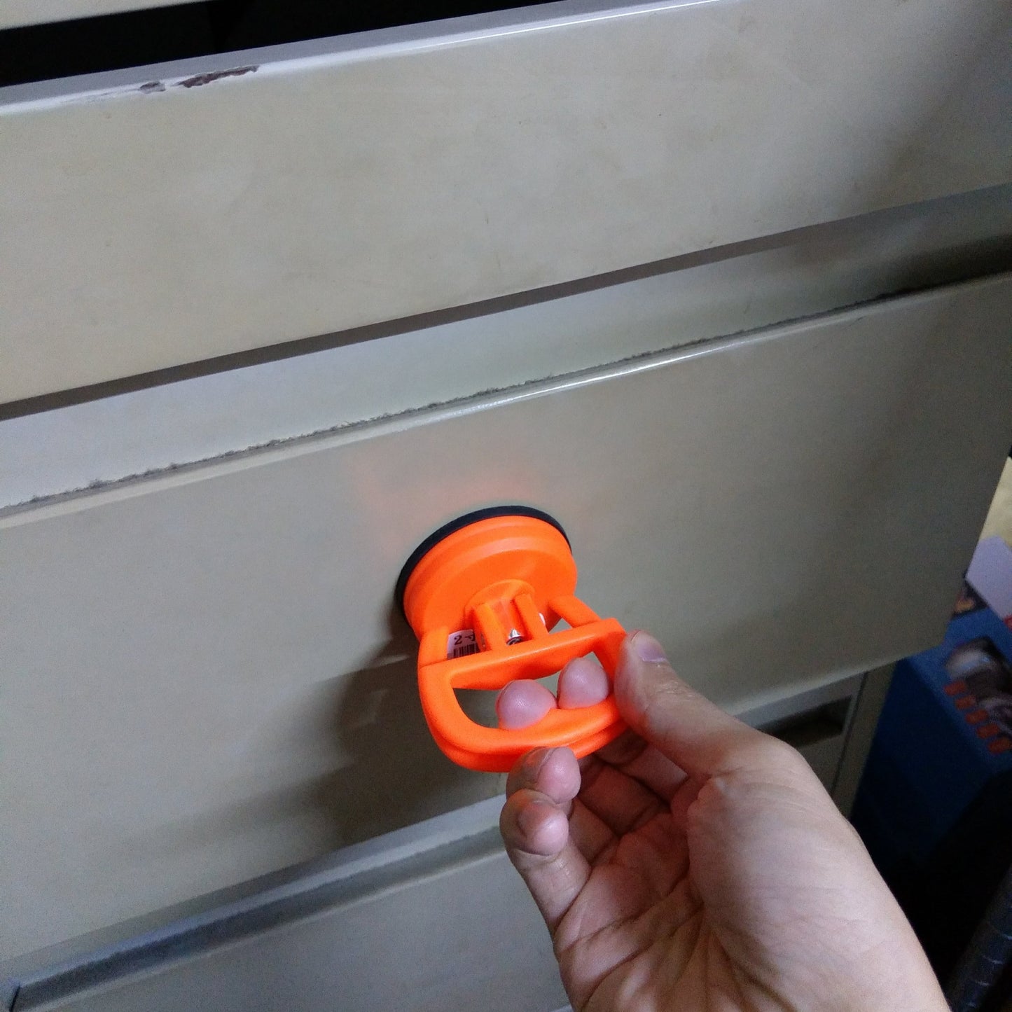 A hand using the mini suction cup to pull open a metal drawer, showcasing its strength.