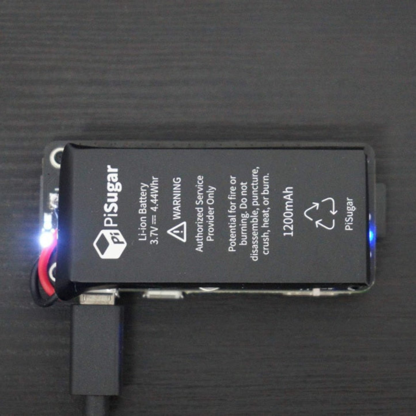 Close-up of the PiSugar2 lithium battery pack highlighting the 1200mAh capacity, warning labels, and illuminated LED status light.