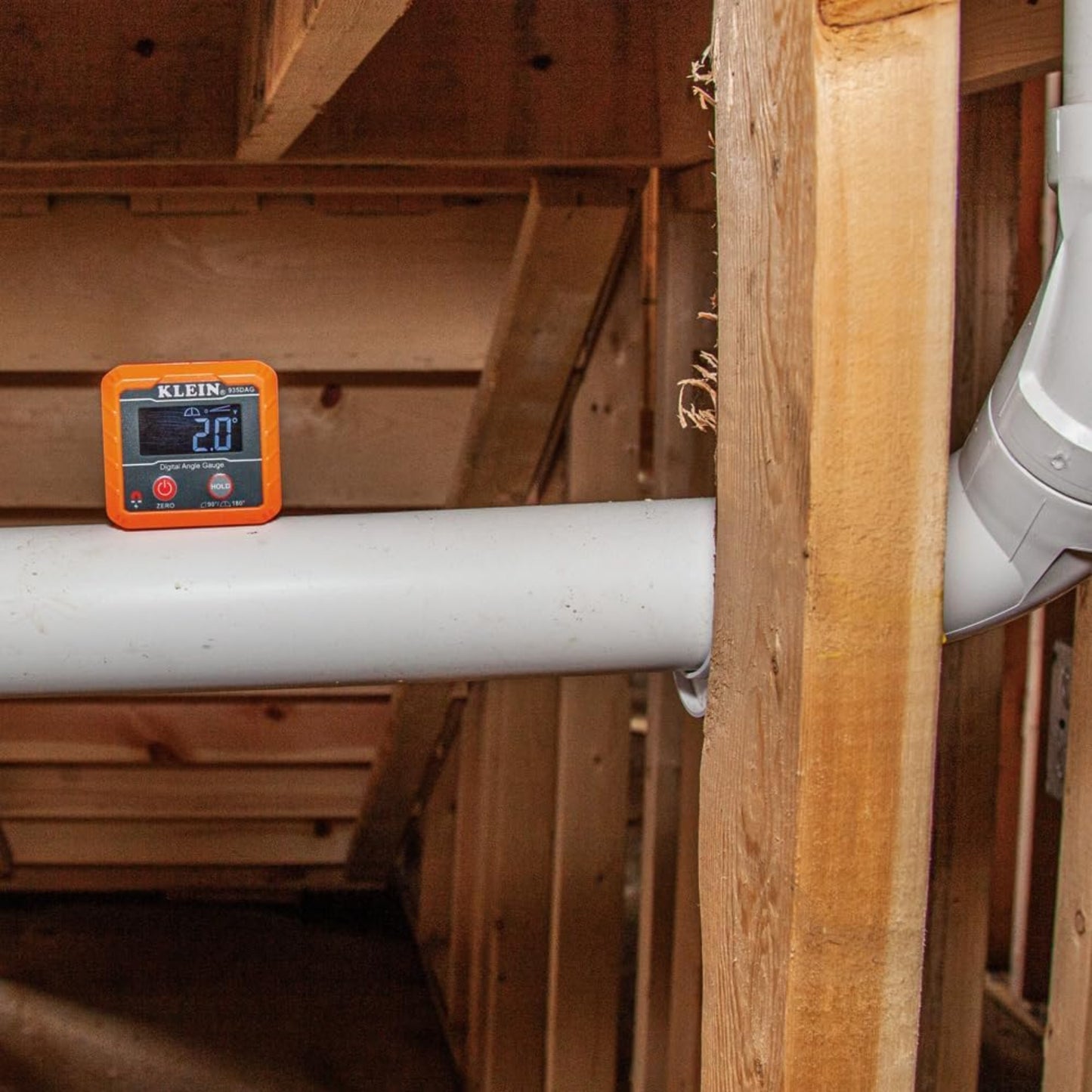 Checking PVC pipe slope in a crawlspace using high visibility digital level.