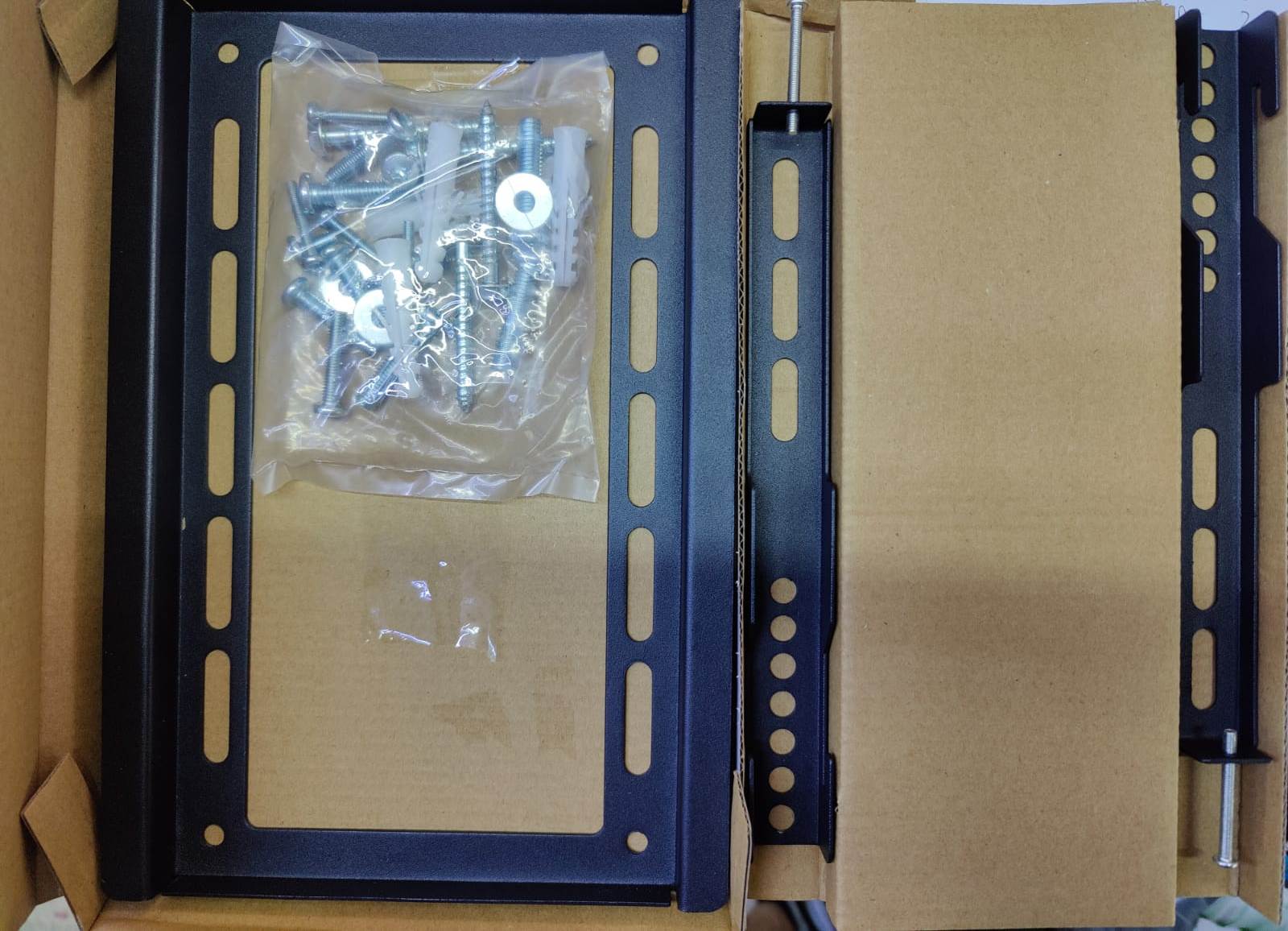 Tiger Mounts SY-F210 電視掛牆架打開的包裝盒，顯示黑色金屬支架及一包用於安裝的螺絲和膨脹管。