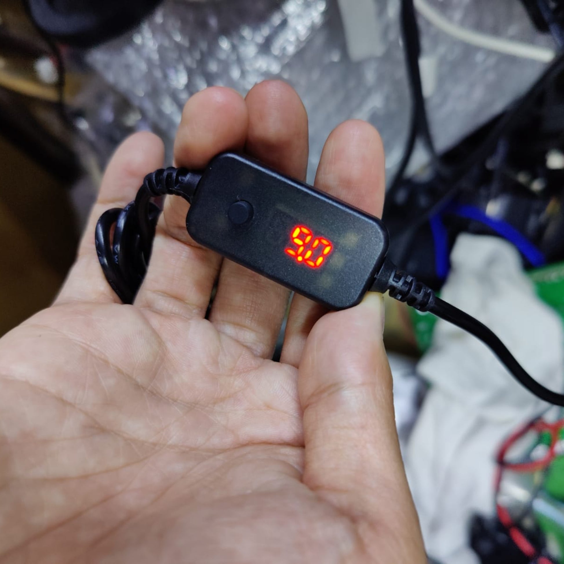 Hand holding a USB-C adjustable voltage cable with a digital display showing 9V output.