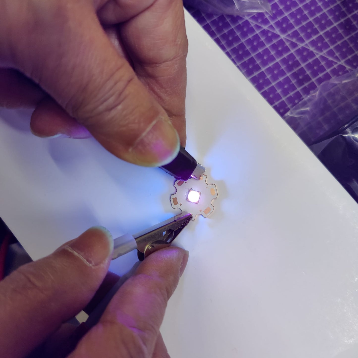 Technician testing 10W UV LED with alligator clips showing violet glow.