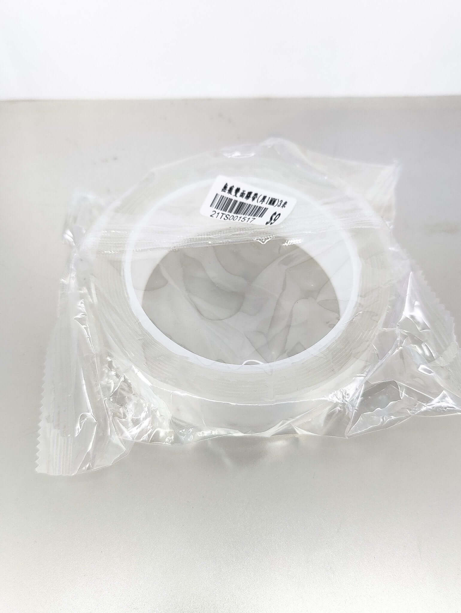 Reusable Nano Adhesive Tape in clear packaging on a silver surface, featuring double-sided sticky sides.