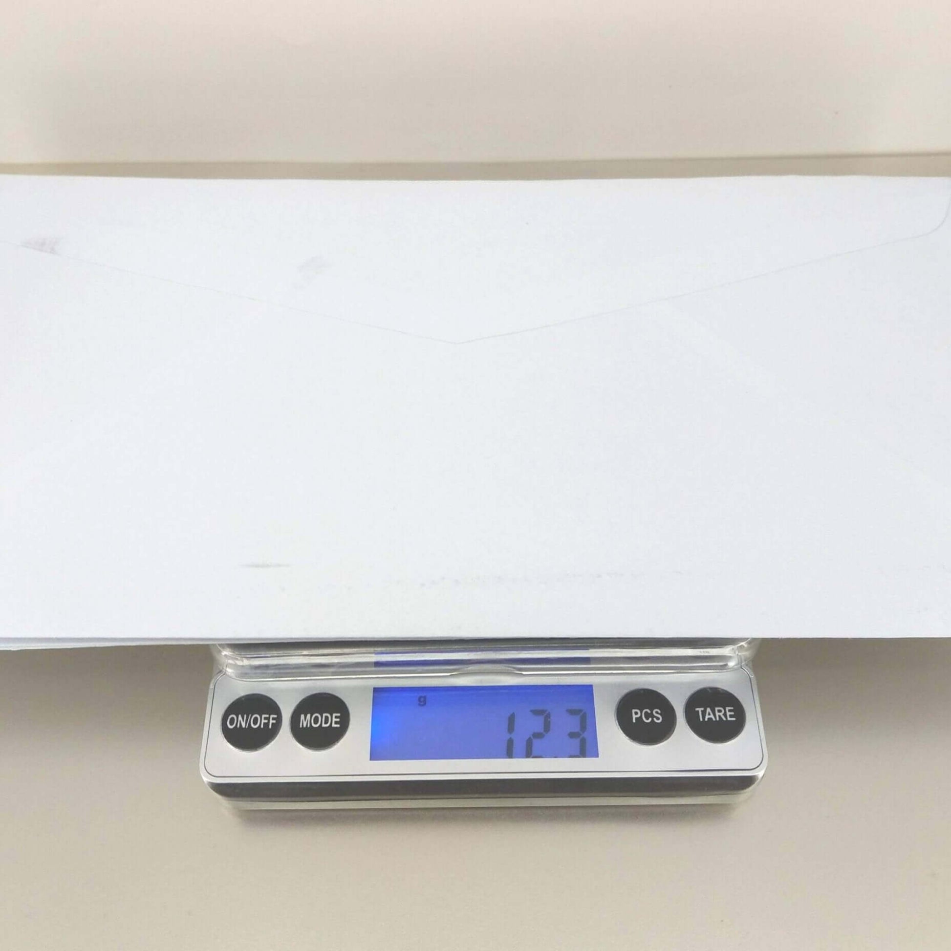 Digital pocket scale showing weight of 123g with an envelope on top, demonstrating high precision and accuracy.