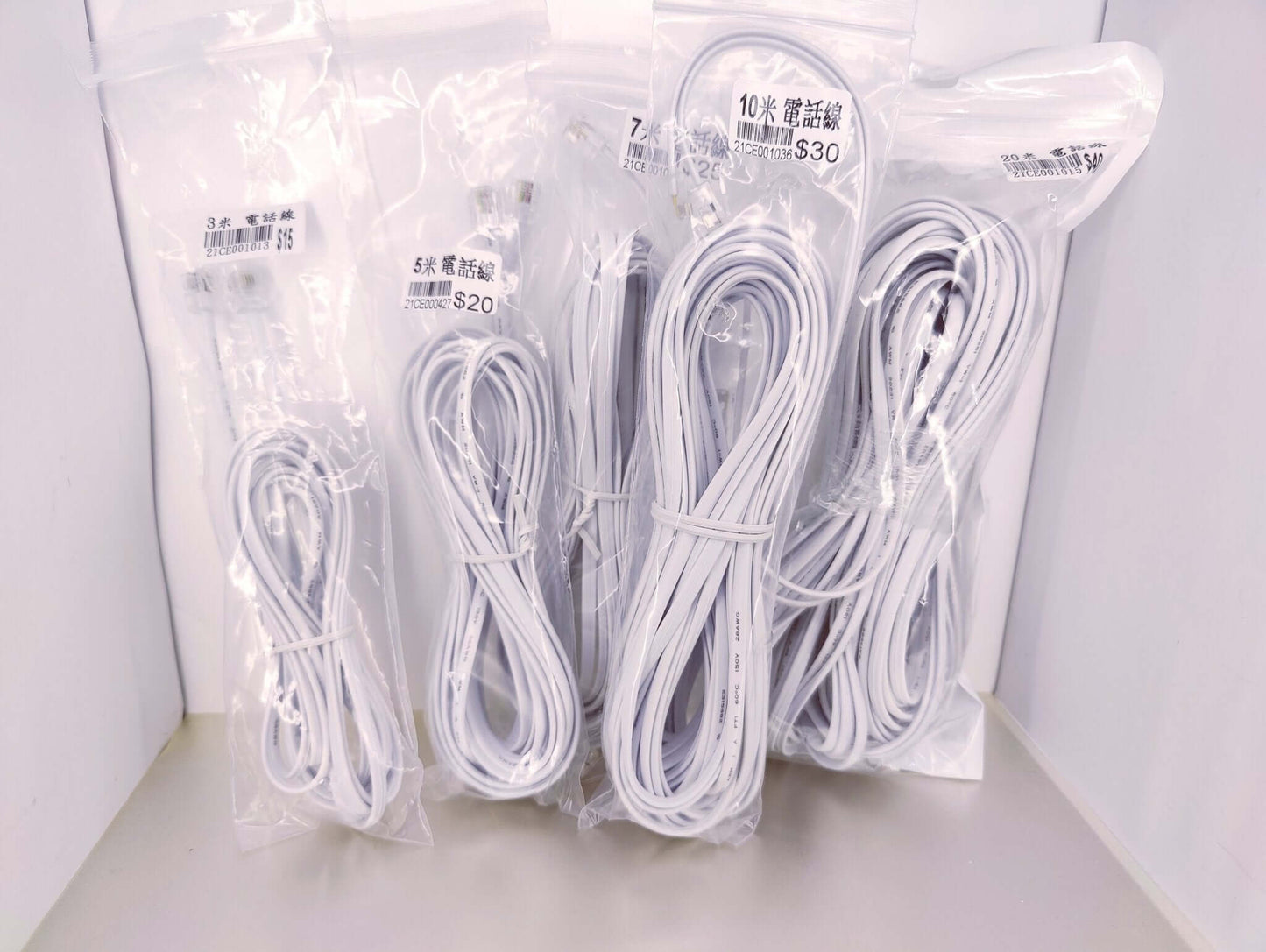 Four packages of white RJ11 telephone extension cables in 3 meter, 5 meter, 10 meter, and 20 meter lengths.