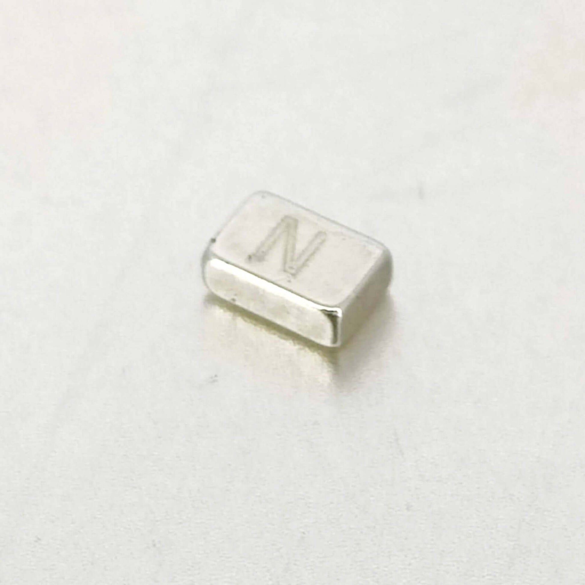 Strong mini rectangular magnet 6x4x2mm with 'N' marking on a smooth surface, ideal for DIY and organizing.