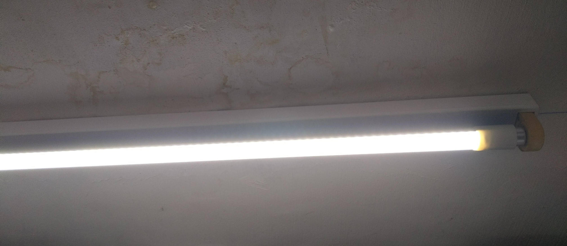 An illuminated T8 48-inch LED tube light installed in a ceiling fixture, emitting bright cool white light into the room.